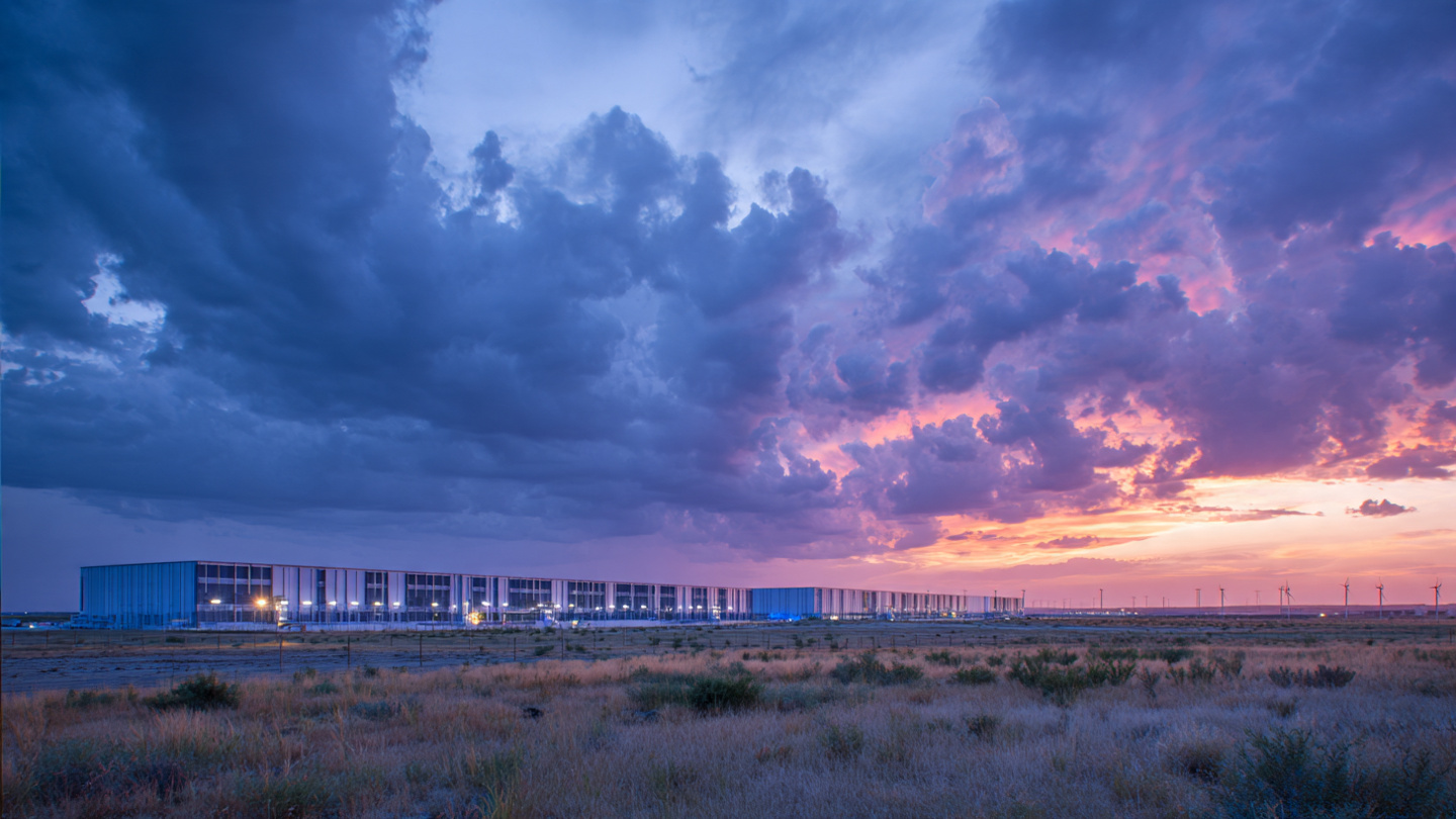 Massive data center complex at twilight with rows of gas turbines alongside solar panels, smoke stacks contrasting with wind turbines on the horizon