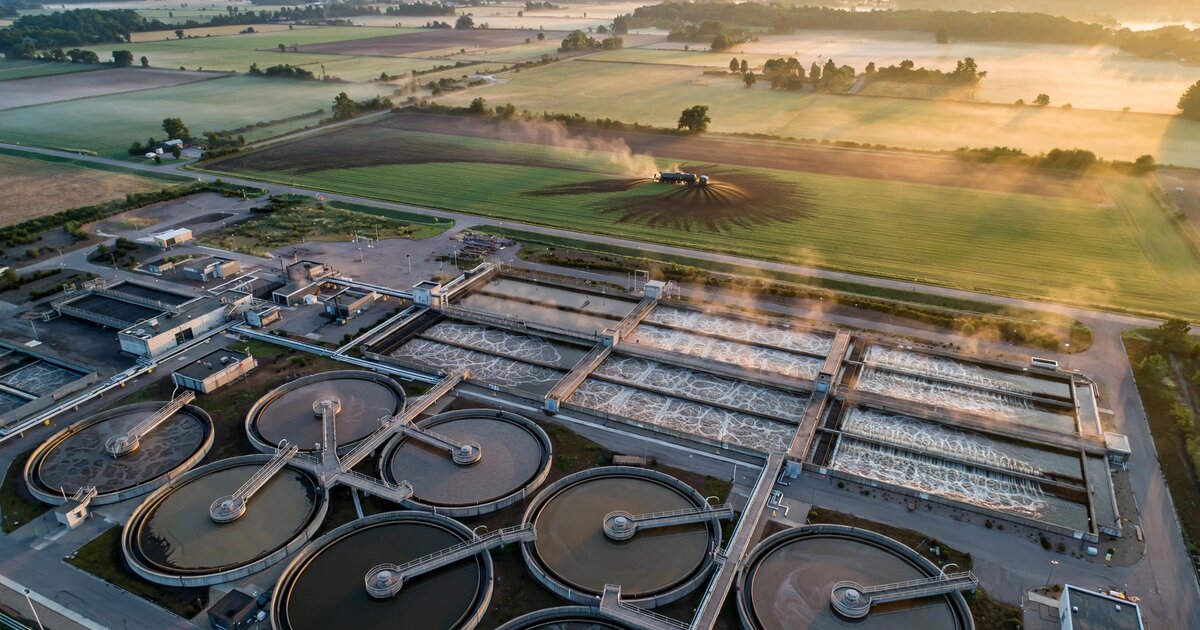 Aerial view of a municipal wastewater treatment facility at dawn with biosolids land application in the background