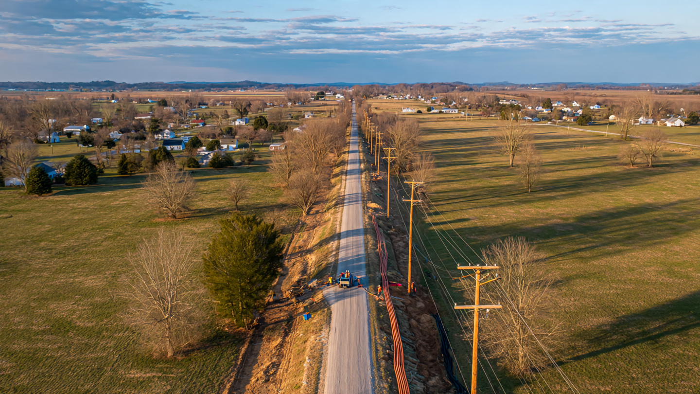 Rural road with utility poles and fiber optic installation crew alongside railroad tracks