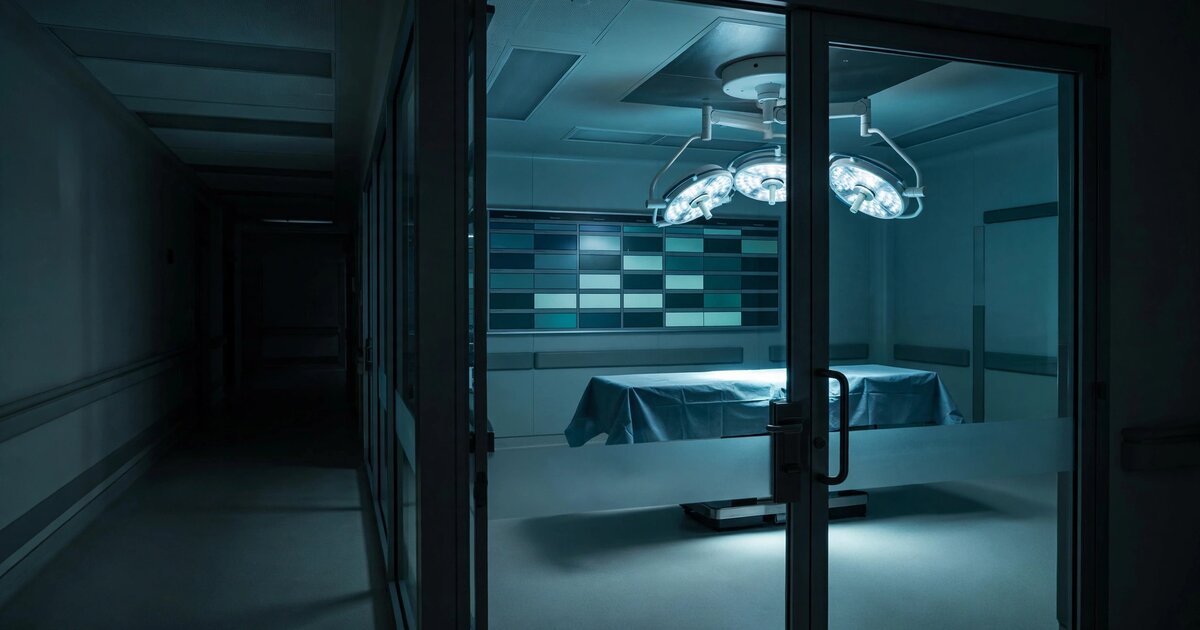 Empty hospital operating room viewed through glass doors with surgical lights illuminating an unused table